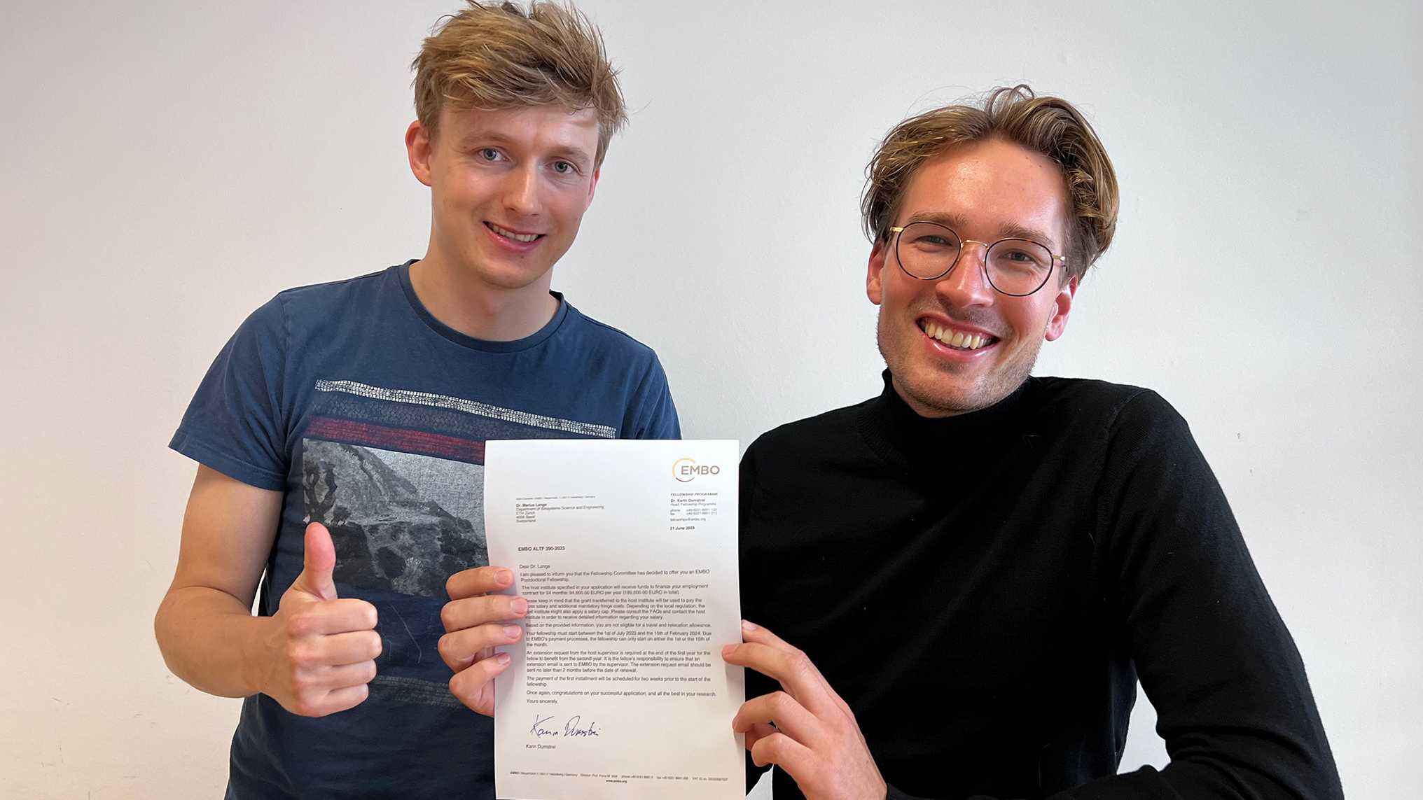 Jasper Janssens and Marius Lange, smiling, holding their EMBO letters into the camera